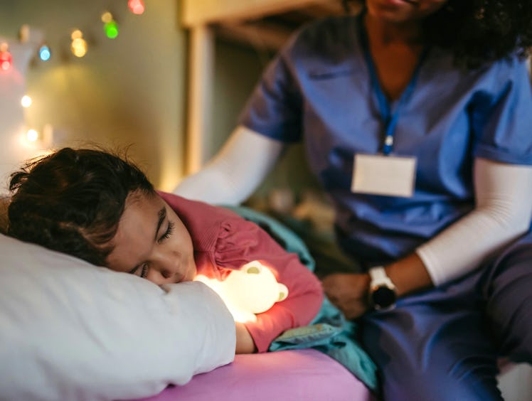 Nurse getting late home from work, stroking sleeping daughter’s hair. Portrait of beautiful doctor w...