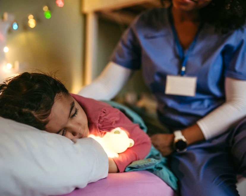 Nurse getting late home from work, stroking sleeping daughter’s hair. Portrait of beautiful doctor w...