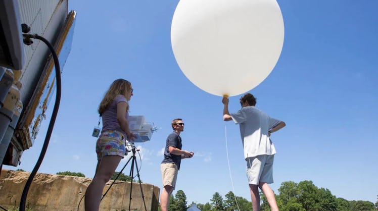 photo of three people holding a large white balloon.