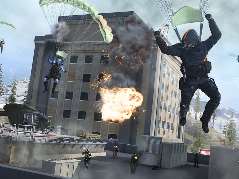 Soldiers with parachutes descend near a building with an explosion, while a helicopter hovers in the...