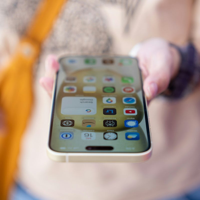 Holding an iPhone 15 Plus with the top of the phone towards the camera and the screen visible.