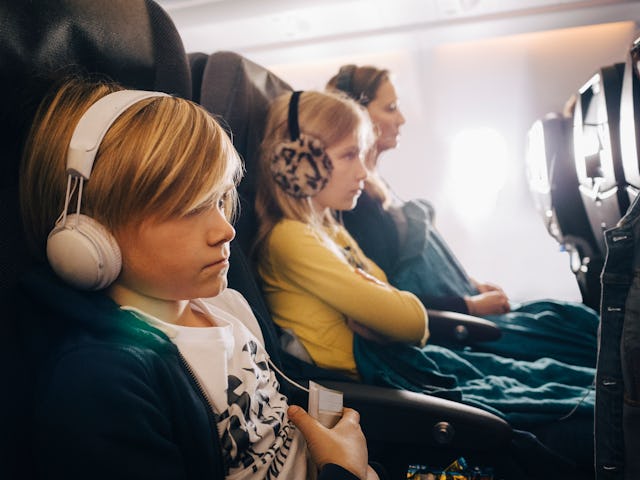 Kids sit next to their mom on an airplane seat.