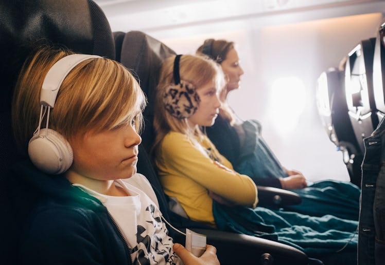 Kids sit next to their mom on an airplane seat.