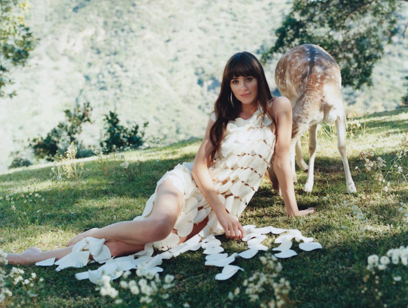 Woman in white dress lies on grass by a deer, with scattered puzzle pieces around her.