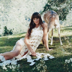 Woman in white dress lies on grass by a deer, with scattered puzzle pieces around her.