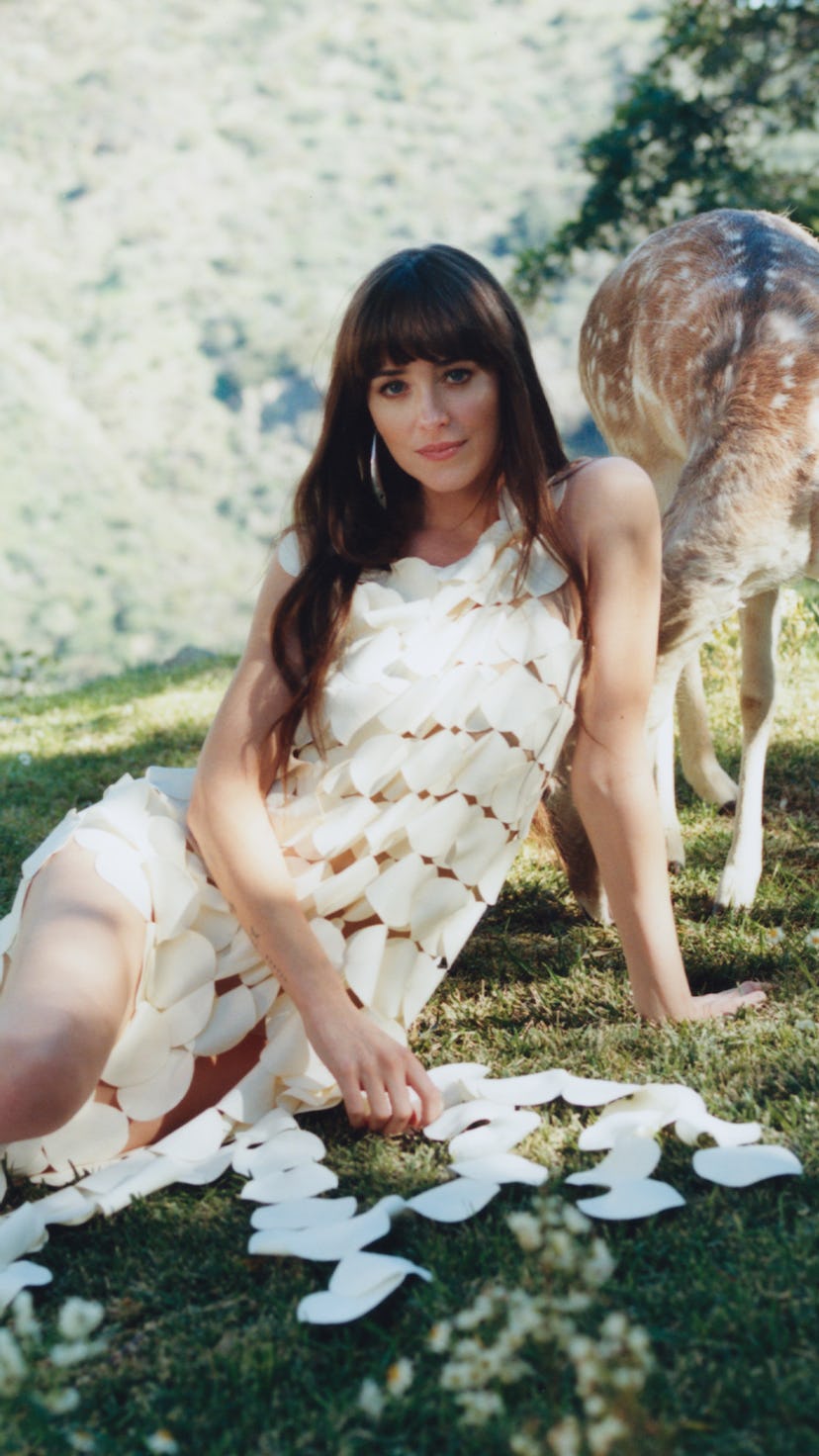 Woman in white dress lies on grass by a deer, with scattered puzzle pieces around her.