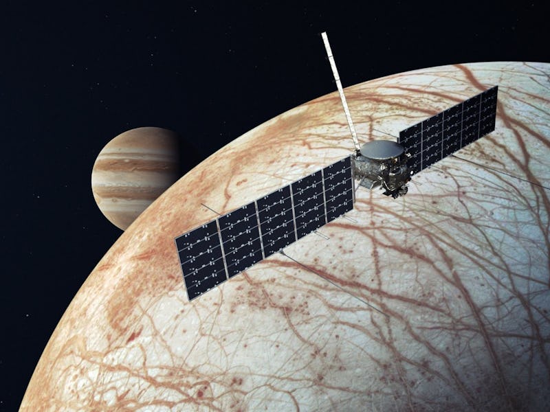 image of a moon with a cracked icy surface, with a satellite in the foreground and Jupiter in the ba...