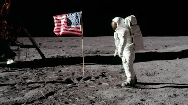 An astronaut stands beside an American flag on the Moon.