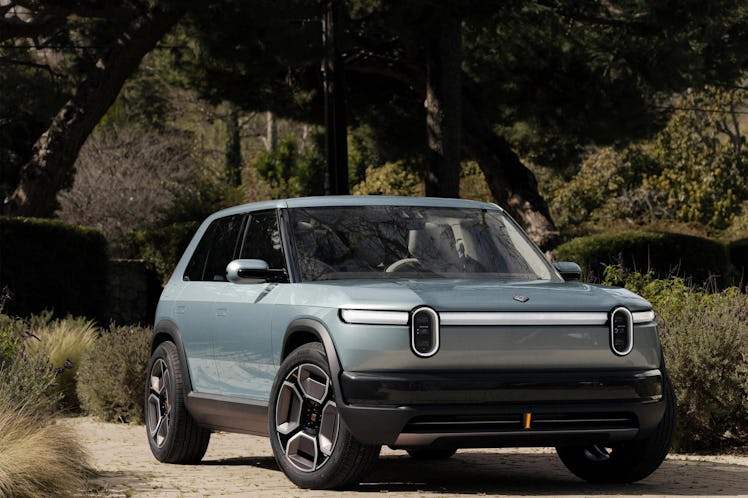 The Rivian R3 parked on a cobblestone driveway in front of trees.