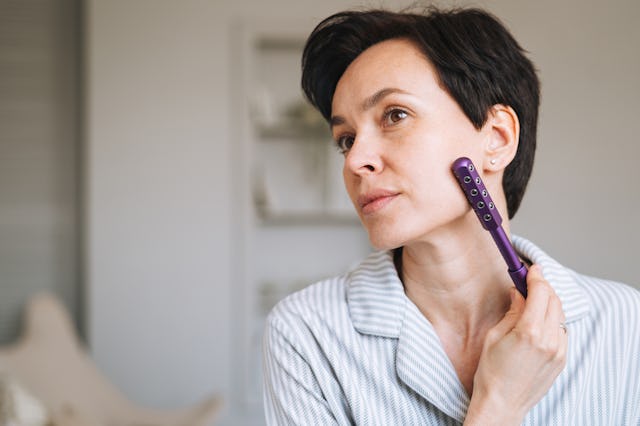 A woman uses a microcurrent device on her face at home.