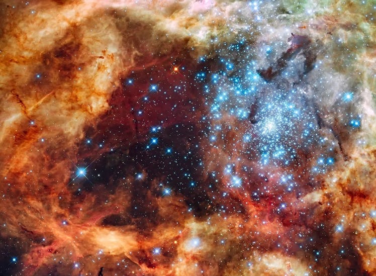 photo of a cluster of bright blue stars surrounded by reddish gas