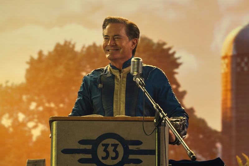 A smiling man at a podium with a microphone, wearing a blue jacket, with a warm sunset and a farm si...