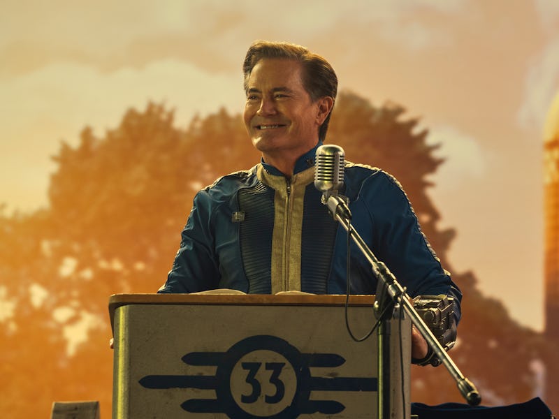 A smiling man at a podium with a microphone, wearing a blue jacket, with a warm sunset and a farm si...