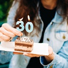 A woman holds a piece of birthday cake with candles.