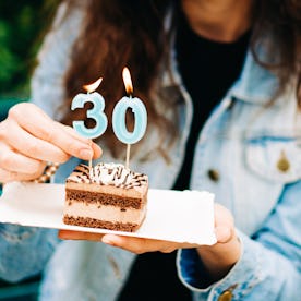 A woman holds a piece of birthday cake with candles.