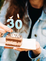 A woman holds a piece of birthday cake with candles.