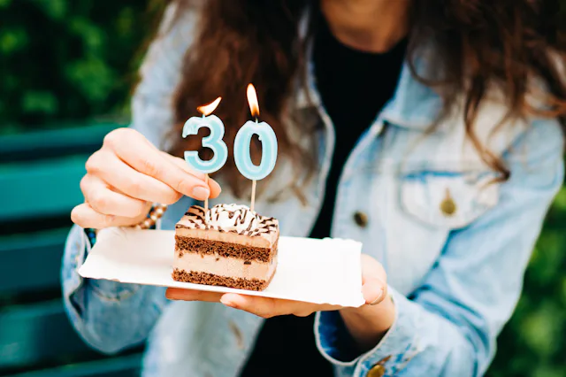 A woman holds a piece of birthday cake with candles.