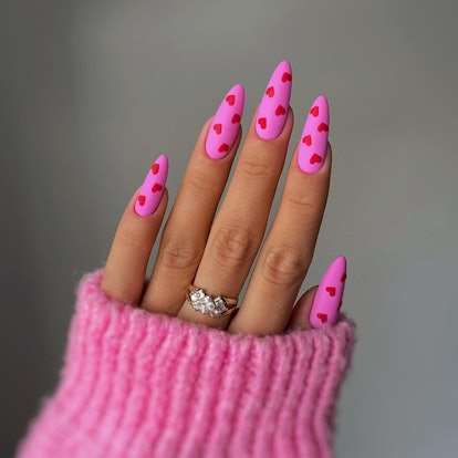 Vibrant pink nails with red hearts are on-trend for 2024.