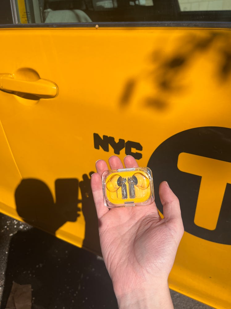 Nothing Ear A wireless earbuds in a hand next to a New York City yellow cab.