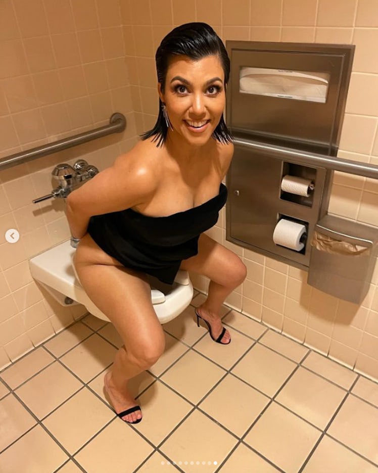 Kourtney Kardashian perched over a toilet wearing a black dress.