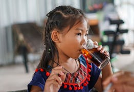Little girl drinks a cola from a glass, in a story answering the question, can kids drink olipop and...