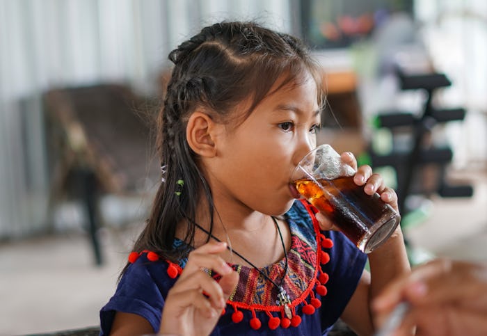 Little girl drinks a cola from a glass, in a story answering the question, can kids drink olipop and...