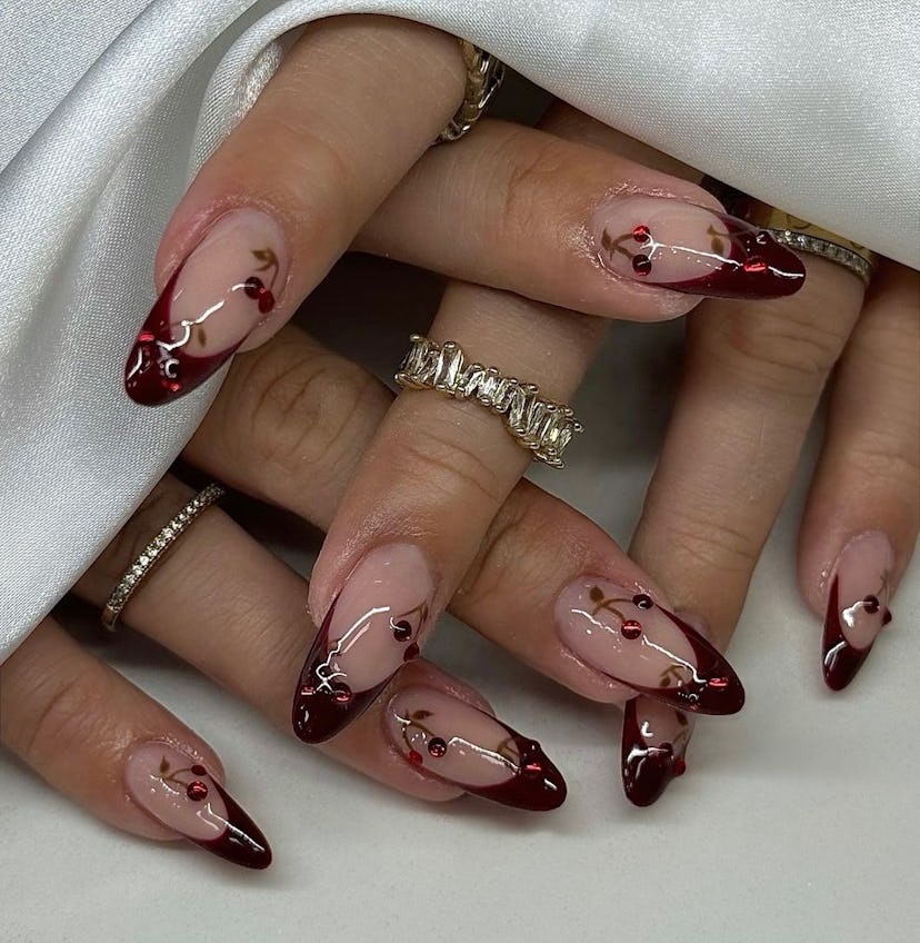 Dark red French tip nails with bedazzled cherry details are on-trend.