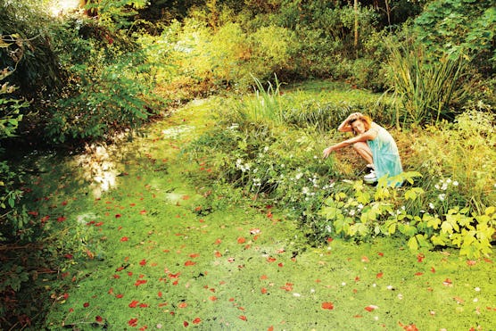 A photograph by Ryan McGinley, styled by Edward Enninful in W July 2013. A model sits in a garden