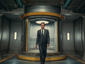 A man in a suit stands confidently in a futuristic circular doorway inside a metallic corridor.