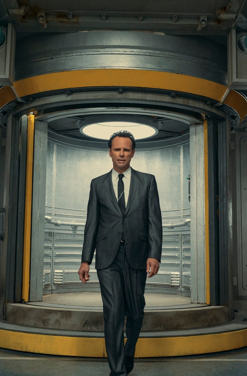A man in a suit stands confidently in a futuristic circular doorway inside a metallic corridor.