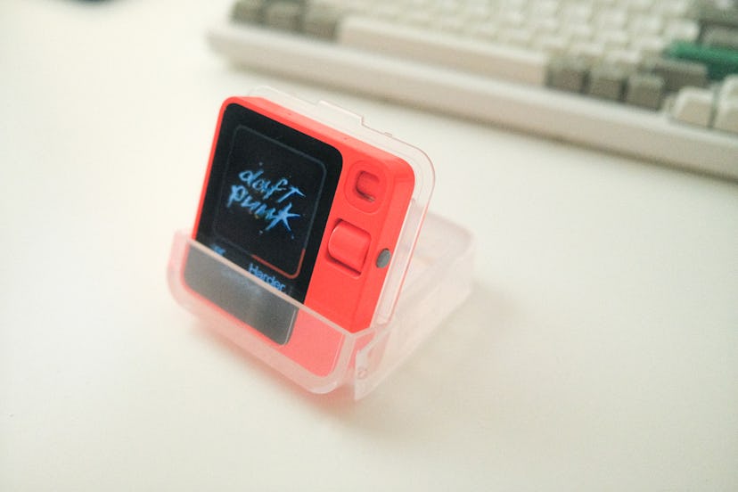 The Rabbit R1 AI gadget in its included plastic case, which doubles as a device stand.