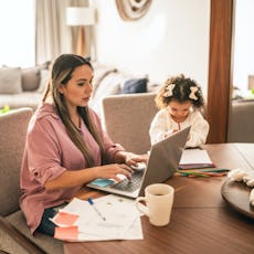 A woman does taxes on her laptop as her daughter sits nearby.