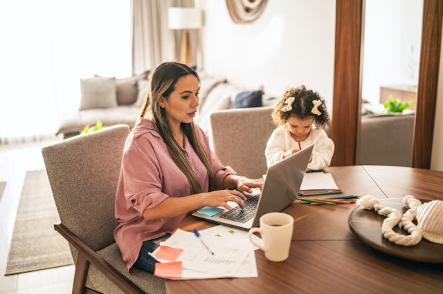 A woman does taxes on her laptop as her daughter sits nearby.