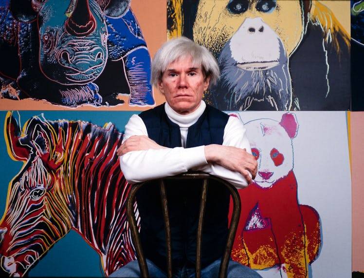American Pop artist Andy Warhol sits in front of several paintings in his 'Endangered Species' at hi...