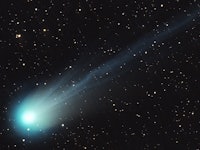 A comet shoots through the sky, it's bright bulb aglow and surrounded by a haze that falls back towa...