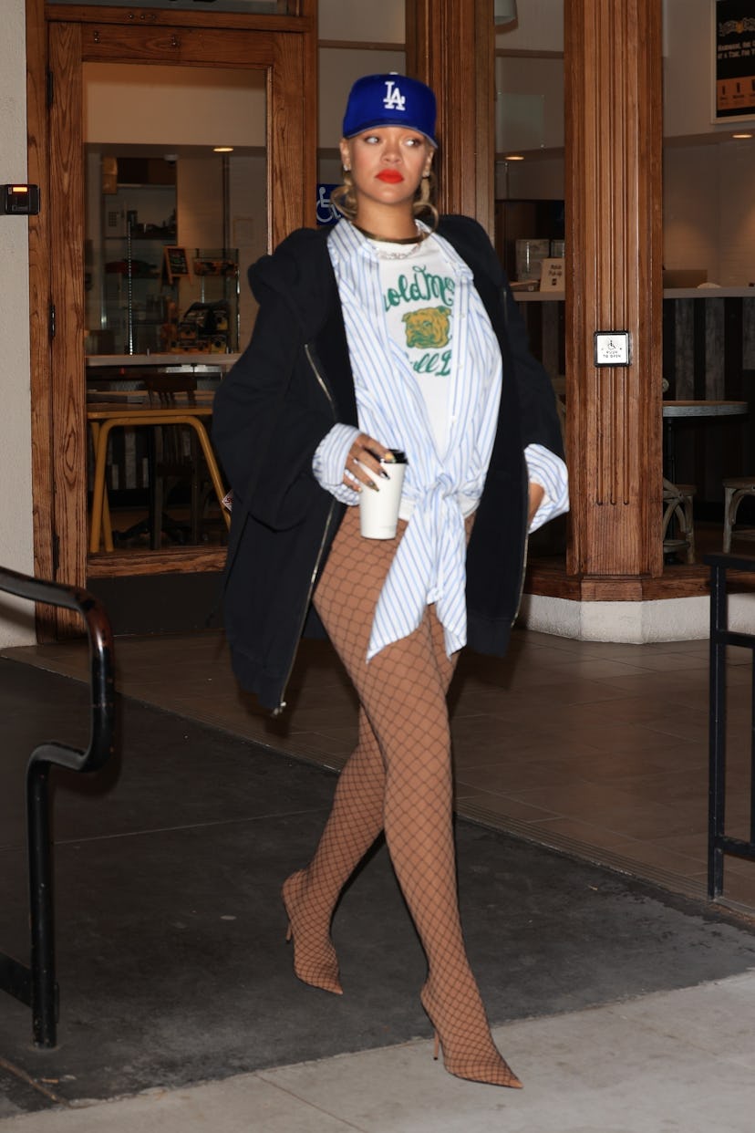 Rihanna wears a graphic tee, hoodie, baseball cap, and pantaboots. 