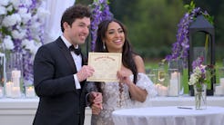 A joyful bride and groom holding a marriage certificate at an elegantly decorated outdoor wedding ve...