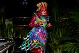 Person in colorful costume with elaborate headdress and ribbons performing at a night event surround...