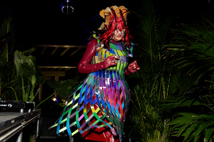 Person in colorful costume with elaborate headdress and ribbons performing at a night event surround...