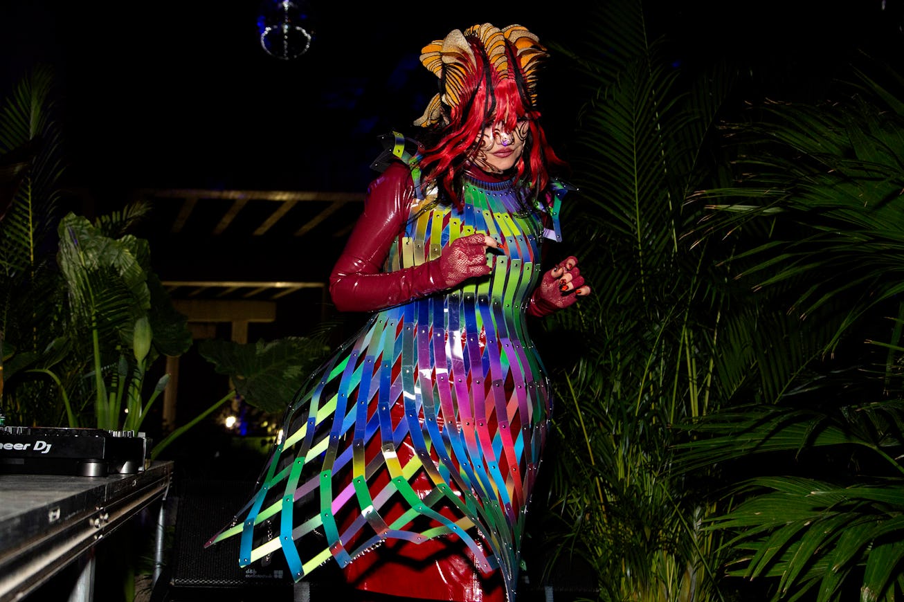 Person in colorful costume with elaborate headdress and ribbons performing at a night event surround...