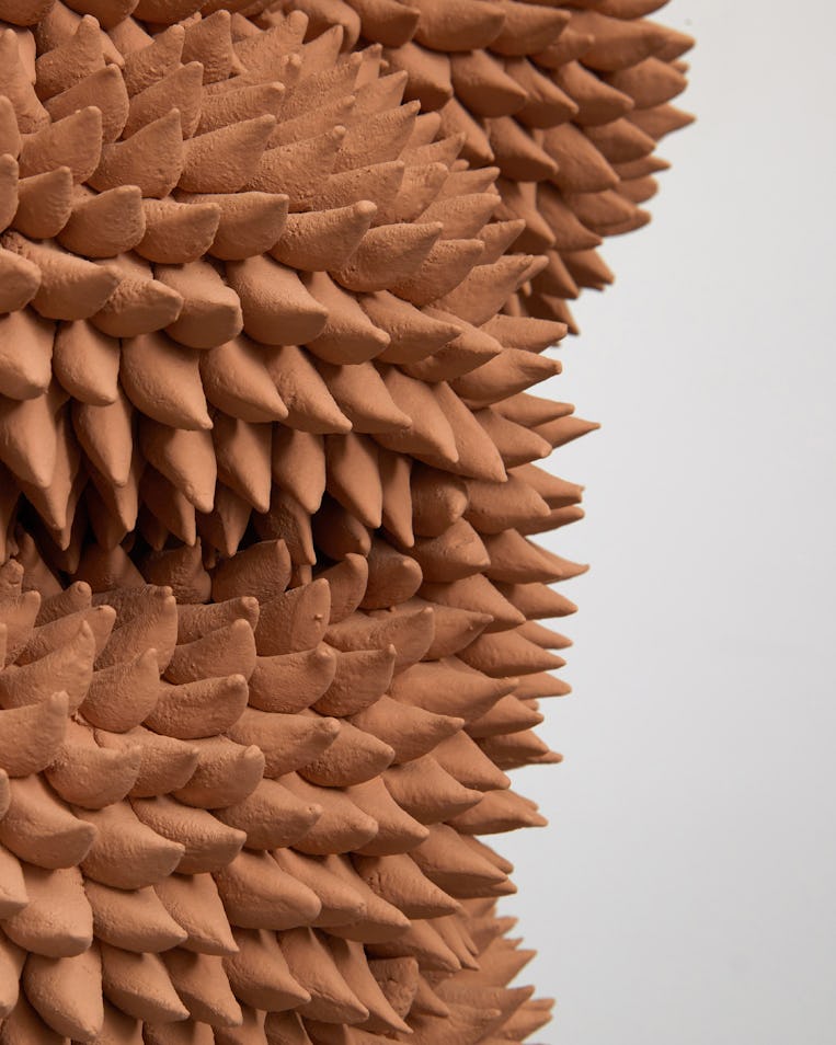 Close-up of a textured sculpture with numerous layered, terracotta colored pointy shapes against a l...