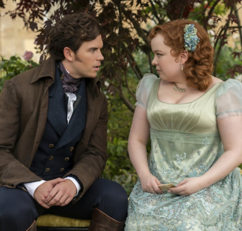 A man and a woman in 19th-century attire sit closely on a bench, engaging in a conversation, surroun...
