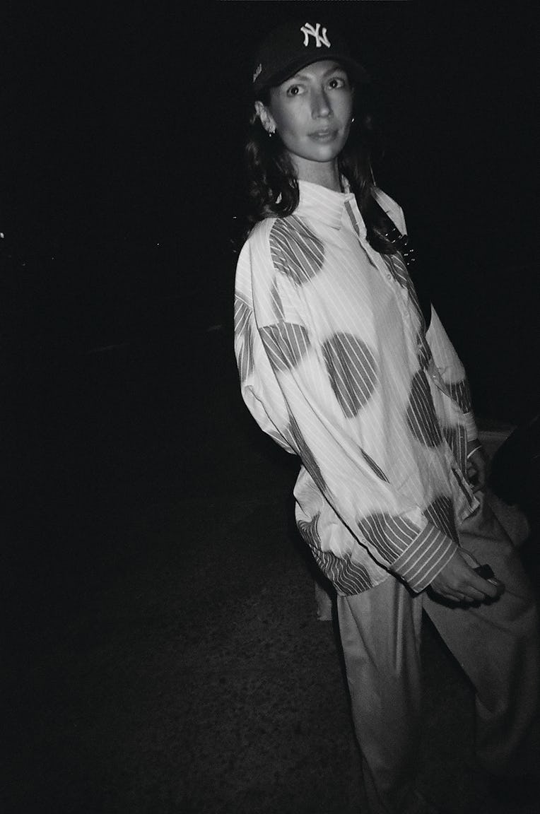 Ashleah Gonzales wearing a NY Yankees cap and a patterned jacket poses at night in a black and white...