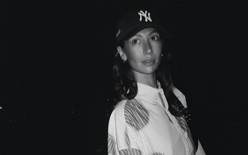 Ashleah Gonzales wearing a NY Yankees cap and a patterned jacket poses at night in a black and white...