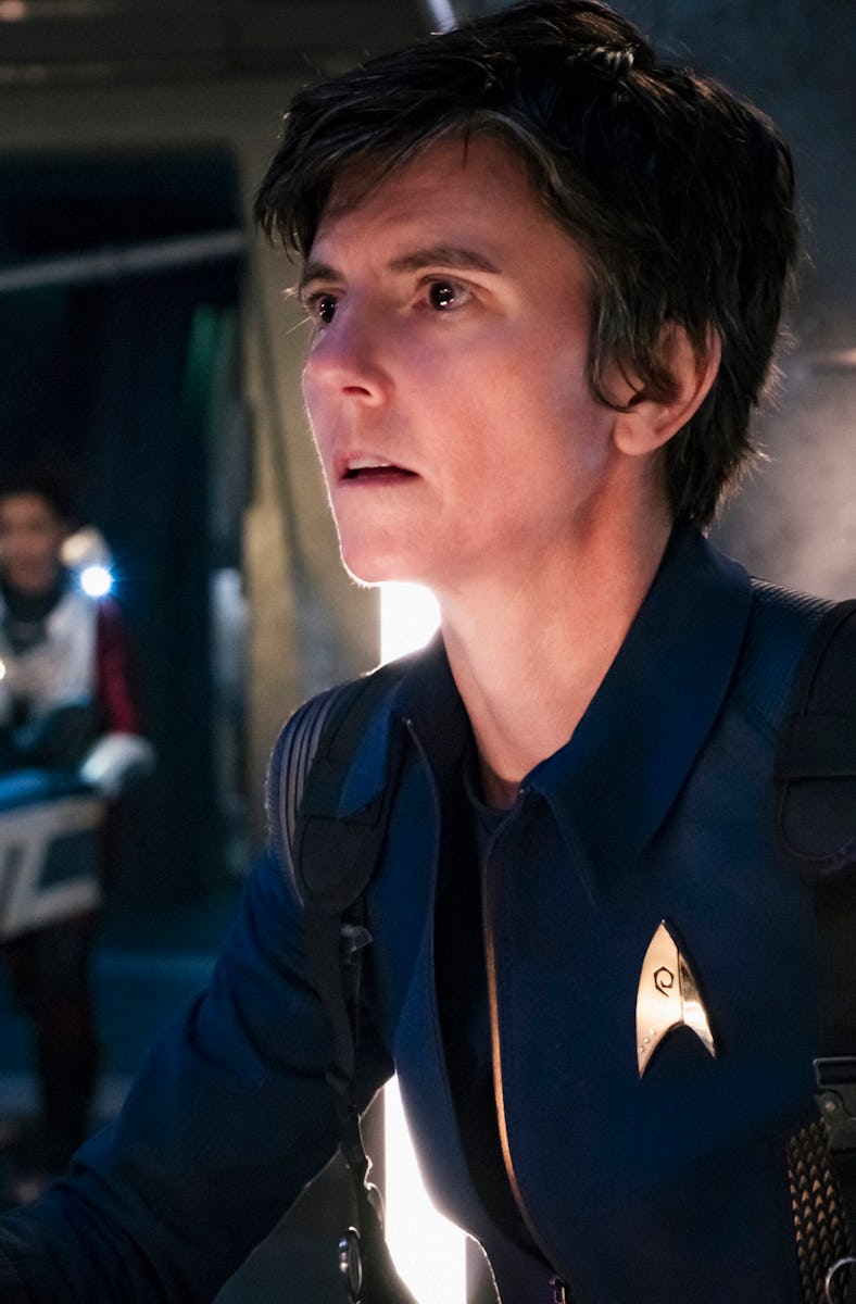 A person in a blue Starfleet uniform looks intently to the side in a dim, futuristic spacecraft sett...