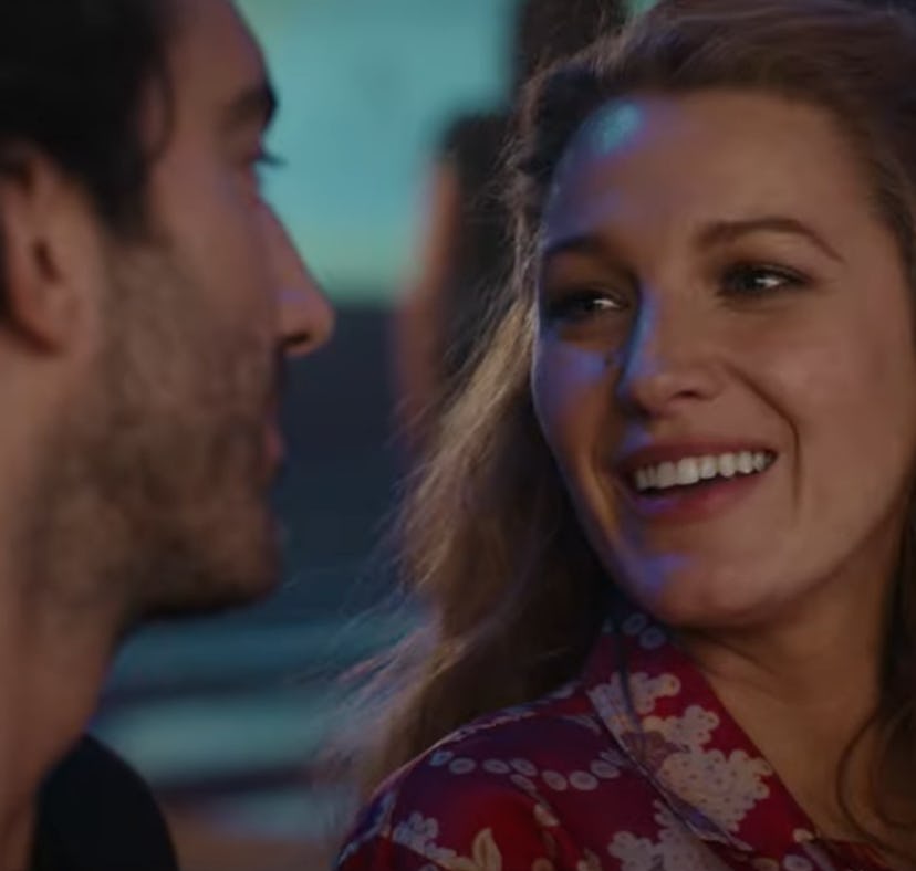 A man and a woman smiling and looking at each other lovingly in a dimly lit room with colorful light...