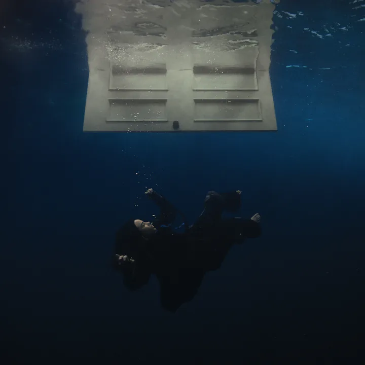 A person in a wet suit floats underwater facing a translucent floating object that reflects light.