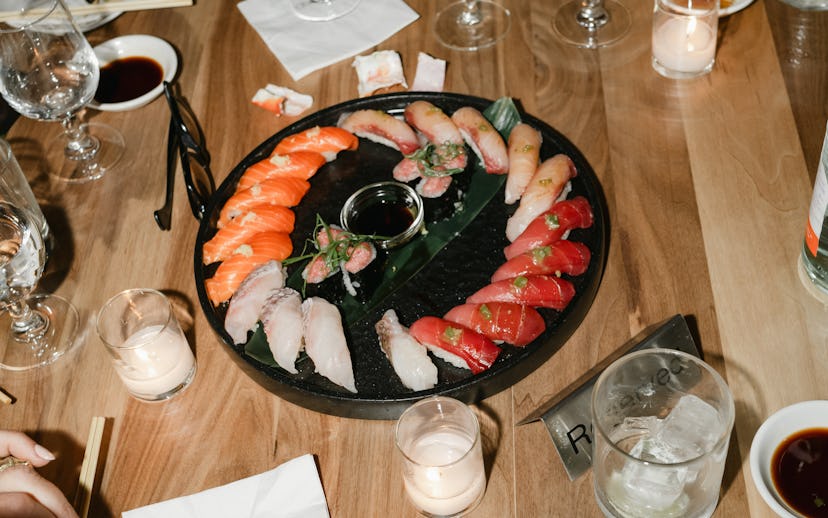 Diners enjoy sushi at a wooden table, with a platter of various sushi types surrounded by drinks and...