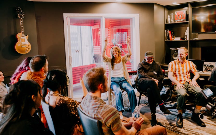 A group of people enjoy a lively gathering in a music-themed room with a guitar hanging on the wall.