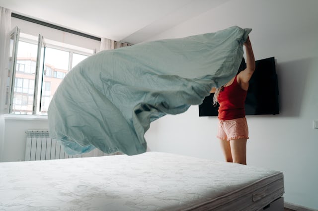 A woman changes the sheets on her bed.